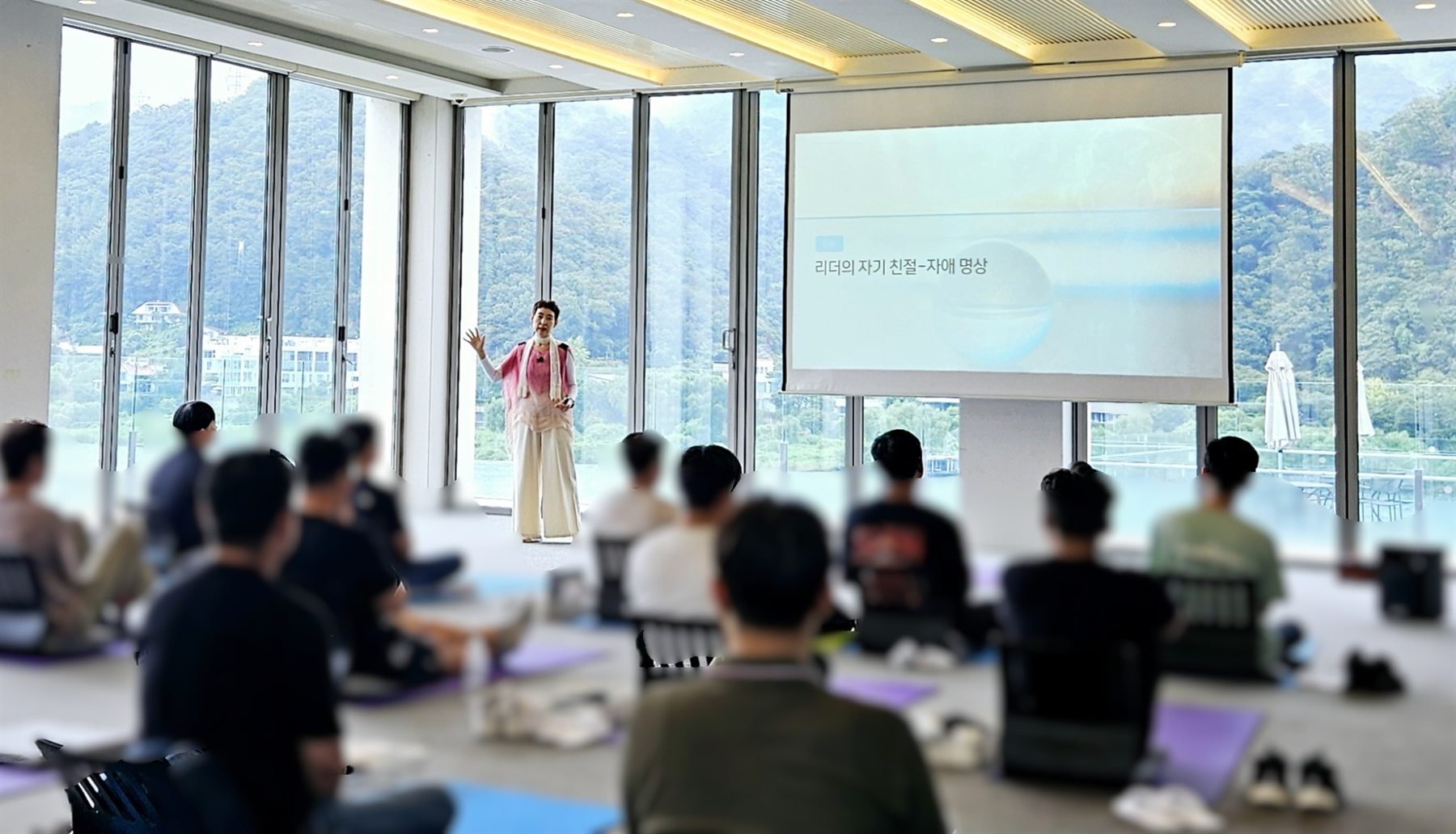 호숫가 리트릿 공간에서 임직원들이 매트에 앉아 ‘리더의 자기 친절·자애 명상’ 세션에 참여하는 모습